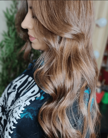 Perfil de mulher exibindo cabelos longos e ondulados com luzes em tons de mel brilhante.