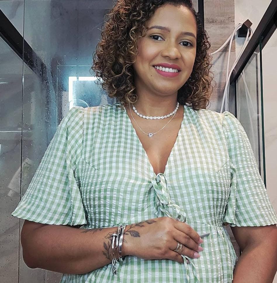 Mulher sorridente de cabelos cacheados usando vestido xadrez verde e branco com acessórios prateados.