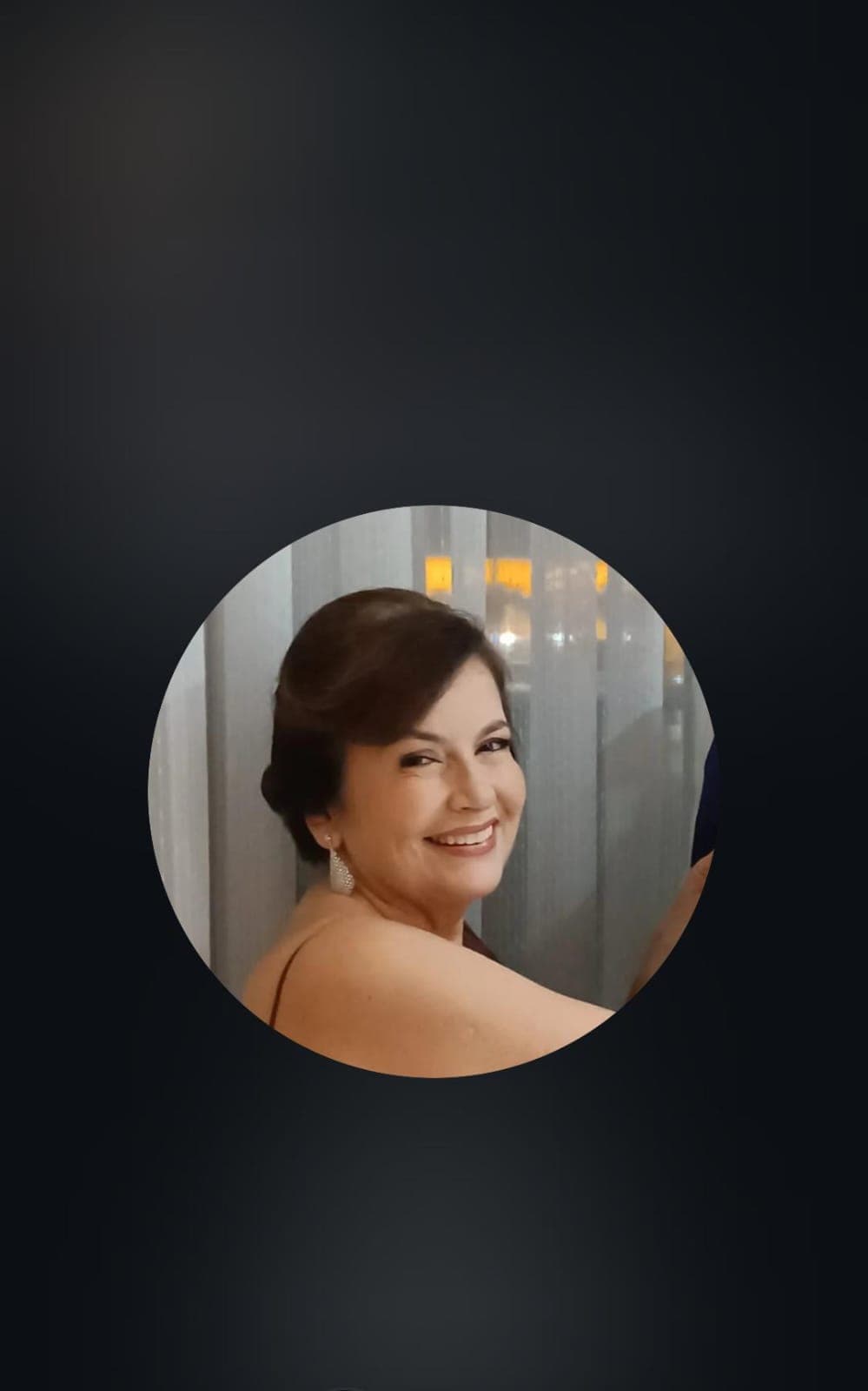 Mulher sorridente de cabelos castanhos e brincos elegantes, emoldurada em um círculo sobre fundo preto.
