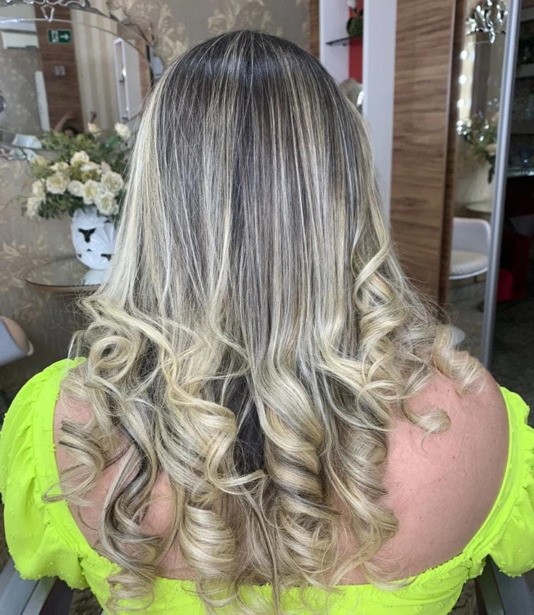 Cabelo longo com mechas loiras, liso na raiz e com cachos definidos nas pontas.